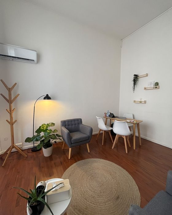 Lo studio visto dall'ingresso: un tappeto rotondo, una poltrona grigia, una lampada, un attaccapanni in legno e un tavolo con due sedie bianche