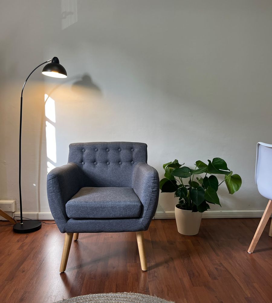 Una poltrona grigia nello studio, accanto a una lampada accesa e a una pianta di monstera